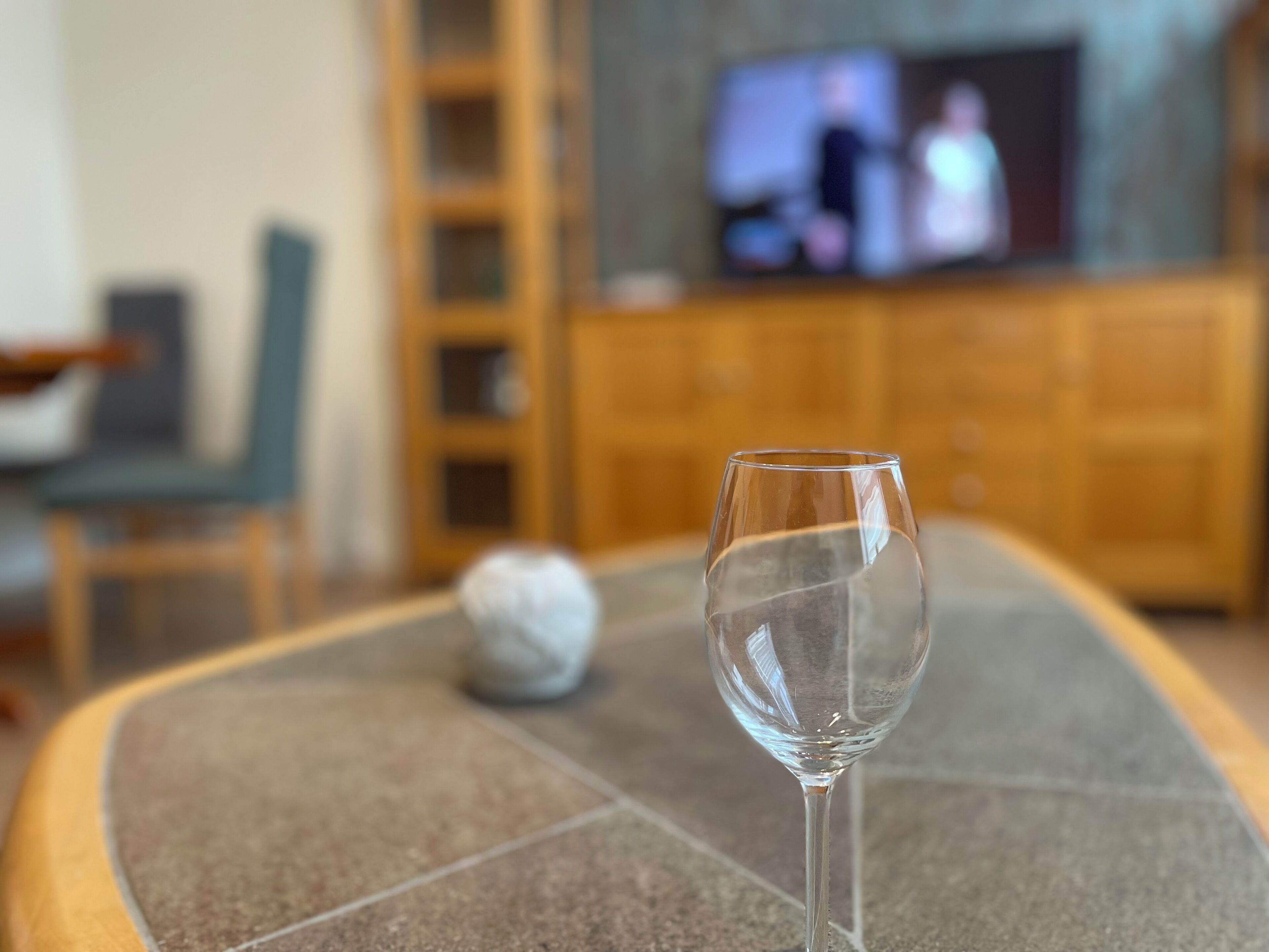 Un bicchiere di vetro trasparente su un tavolo piastrellato, con una televisione sullo sfondo.