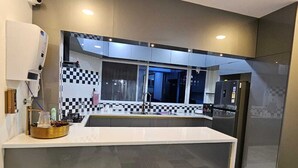 A modern kitchen with a large island, a checkered backsplash, and a view into the adjacent living area. - SS LUMINA GUEST HOUSE (Bengaluru)