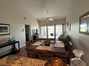 Relax in this open-plan living space with a dining area and seating area, featuring a ceiling fan, TV, and large window.