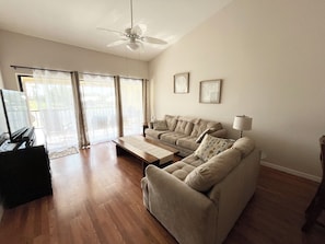 Relax in this spacious living room with a high ceiling, featuring a large sofa, coffee table, and television.