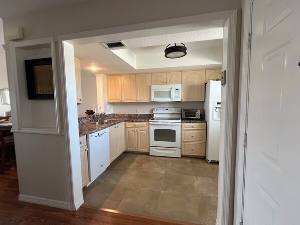 Kitchen area with oven, microwave, and refrigerator, featuring a granite countertop and stainless steel sink.