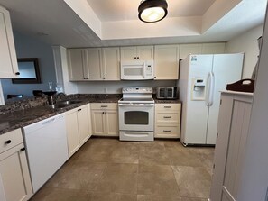 Una cocina con armarios blancos, microondas, tostadora, refrigerador y lavavajillas.