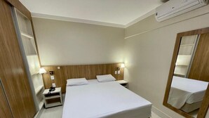 Ein Hotelzimmer mit einem großen Bett, Nachttischlampen, einem Beistelltisch, einem Spiegel und einer Klimaanlage.