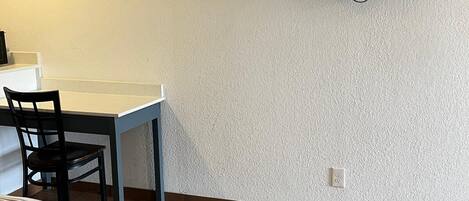 Una habitación con piso de madera, una cama con manta a rayas, un escritorio con silla y un televisor montado en la pared.