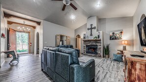 A spacious living room with a stone fireplace, leather seating, and a large painting. - Toasted Marshmallows | Luxury Cabin in Ruidoso w/ Hot Tub & Game Room (Ruidoso)
