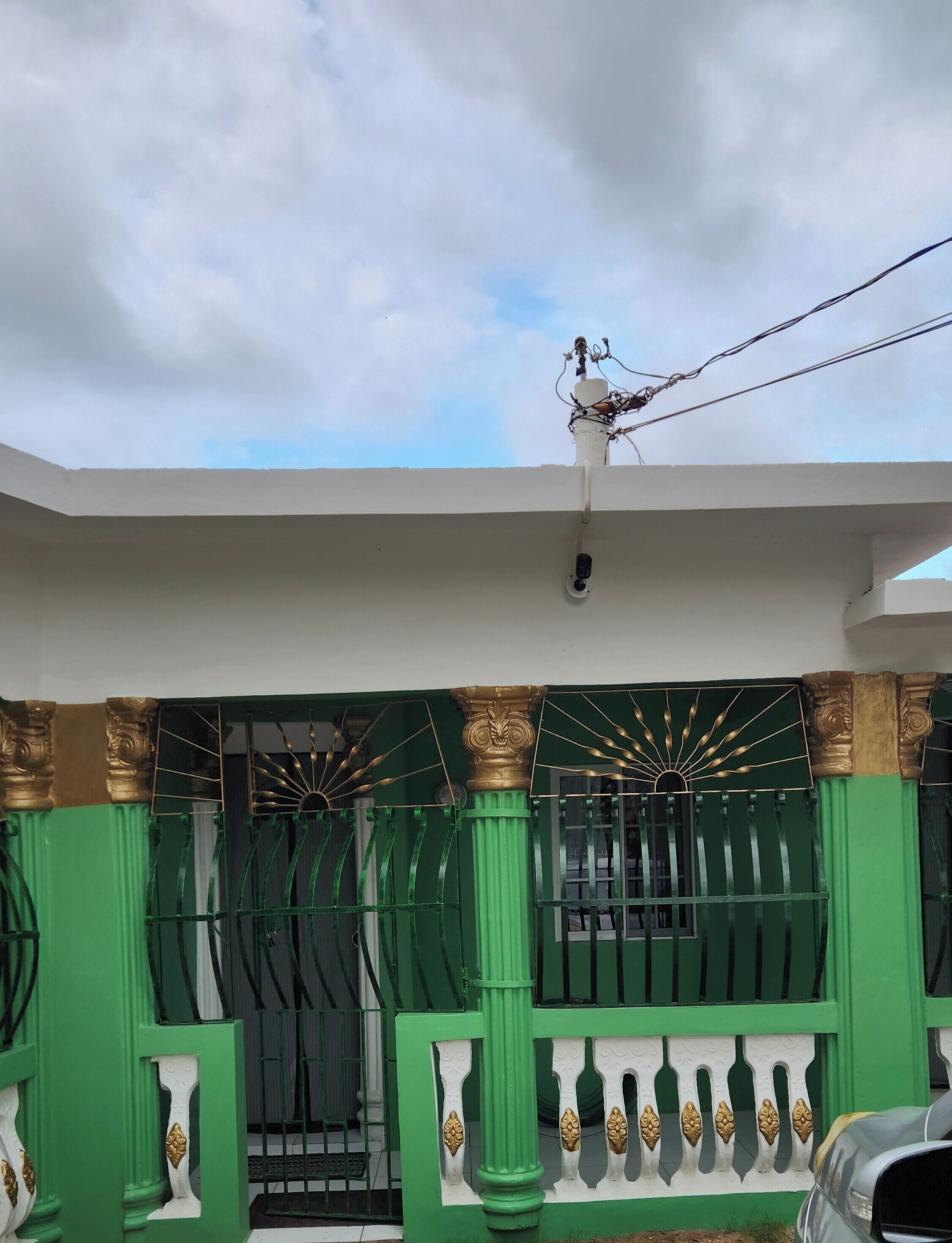 A gated entrance with green and gold decorative elements, a white wall, and a clear sky.