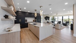A modern kitchen with a central island, black cabinetry, and a large window providing natural light. - Lido Luxe Estate: Large Rental Steps to the Beach with Pool, Spa, Outdoor Games (Lido Key)