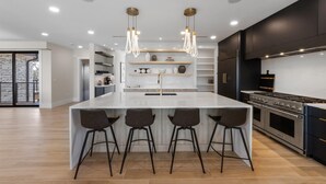A modern kitchen with a central island, bar stools, a built-in oven, and pendant lighting. - Lido Luxe Estate: Large Rental Steps to the Beach with Pool, Spa, Outdoor Games (Lido Key)