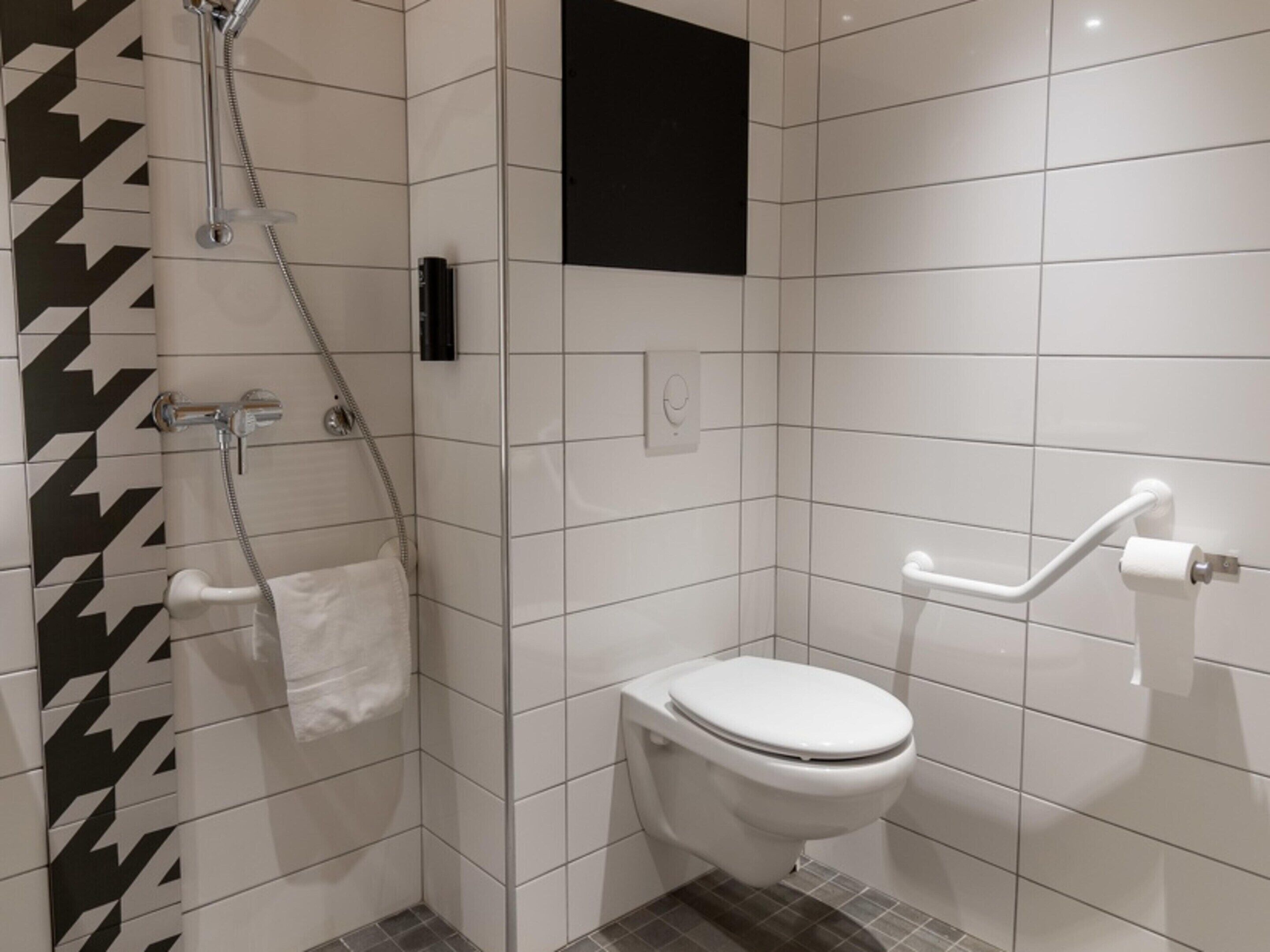 Une salle de bain moderne équipée d’une douche, de toilettes et d’une barre d’appui.