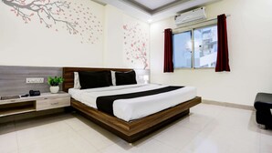 A modern hotel room with a wooden bed, a nightstand, a desk, a potted plant, and a window with red curtains.