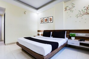 A modern hotel room with a large bed, bedside tables, a nightstand, a wall-mounted telephone, and a small potted plant. - Super Townhouse Hoshangabad Road Near Aashima Mall (Bhopal)