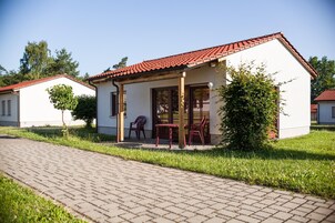 Um pequeno edifício com telhado telhado, varanda coberta com cadeiras e um caminho pavimentado.