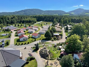 A residential area with multiple houses, a central road, and a mountainous backdrop. - Ferienhaus im Trixi Ferienpark (Grossschoenau)