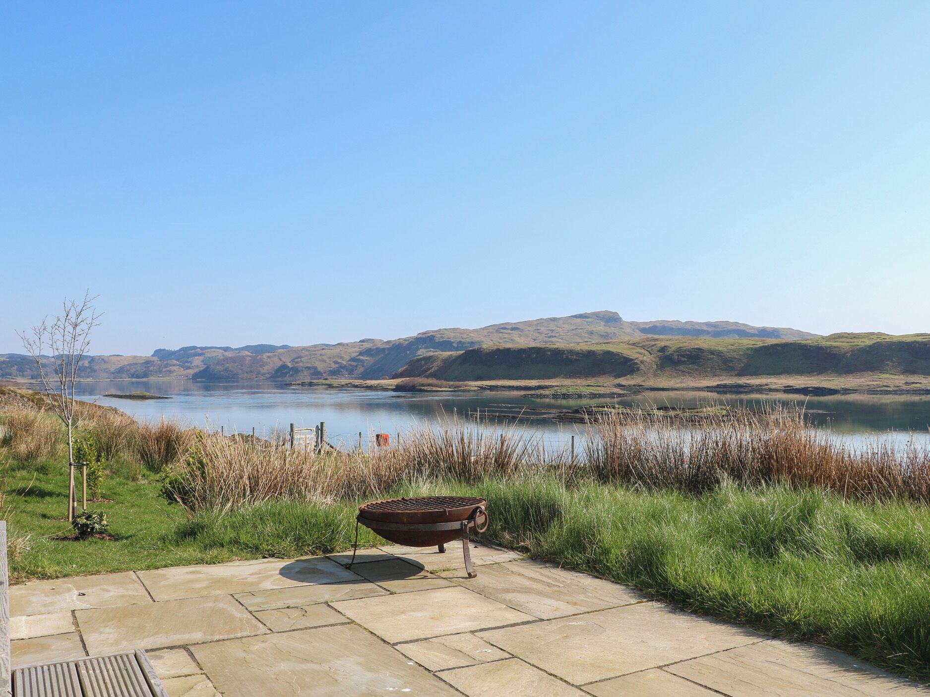 Un patio con una parrilla y vistas a un lago y colinas.