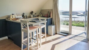 A kitchen with a view of a lake, a dining area with chairs, and a small island with a toaster. - Torsa (Oban)