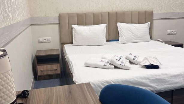 A hotel room with a bed, a desk with a coffee maker, a chair, and a painting on the wall. - Premium 777 (Tashkent)
