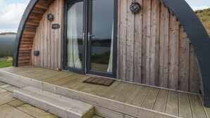 A wooden structure with a curved roof, a glass door, and a small outdoor area with steps. - Creags (Oban)