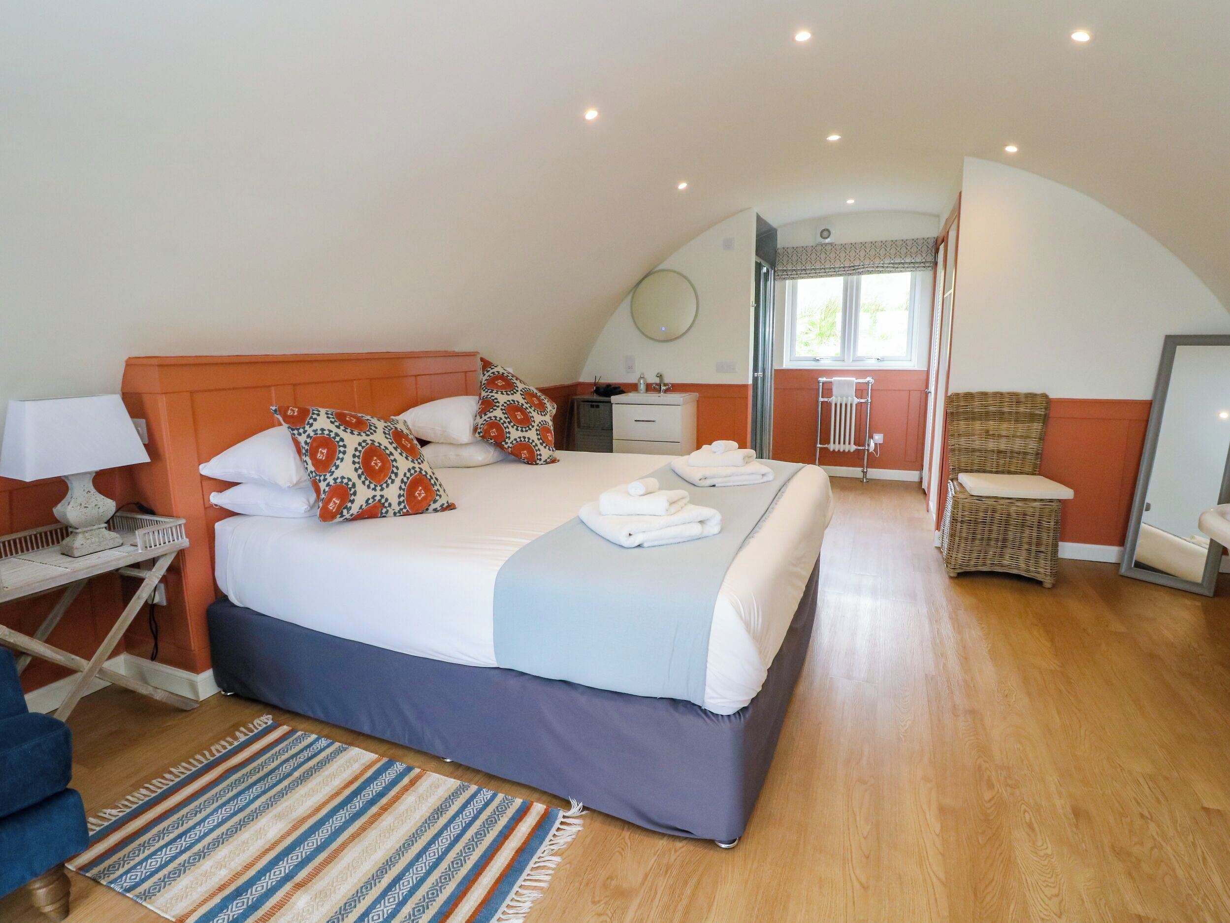 A bedroom with a bed, a nightstand, a chair, a mirror, and a window.