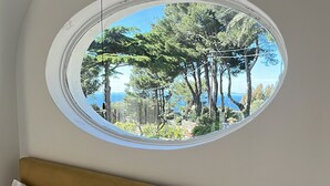 A bedroom with a bed, two pillows with starfish designs, and a round window offering a view of trees and a clear sky. - La Canostra Capri - luxury villa (Anacapri)