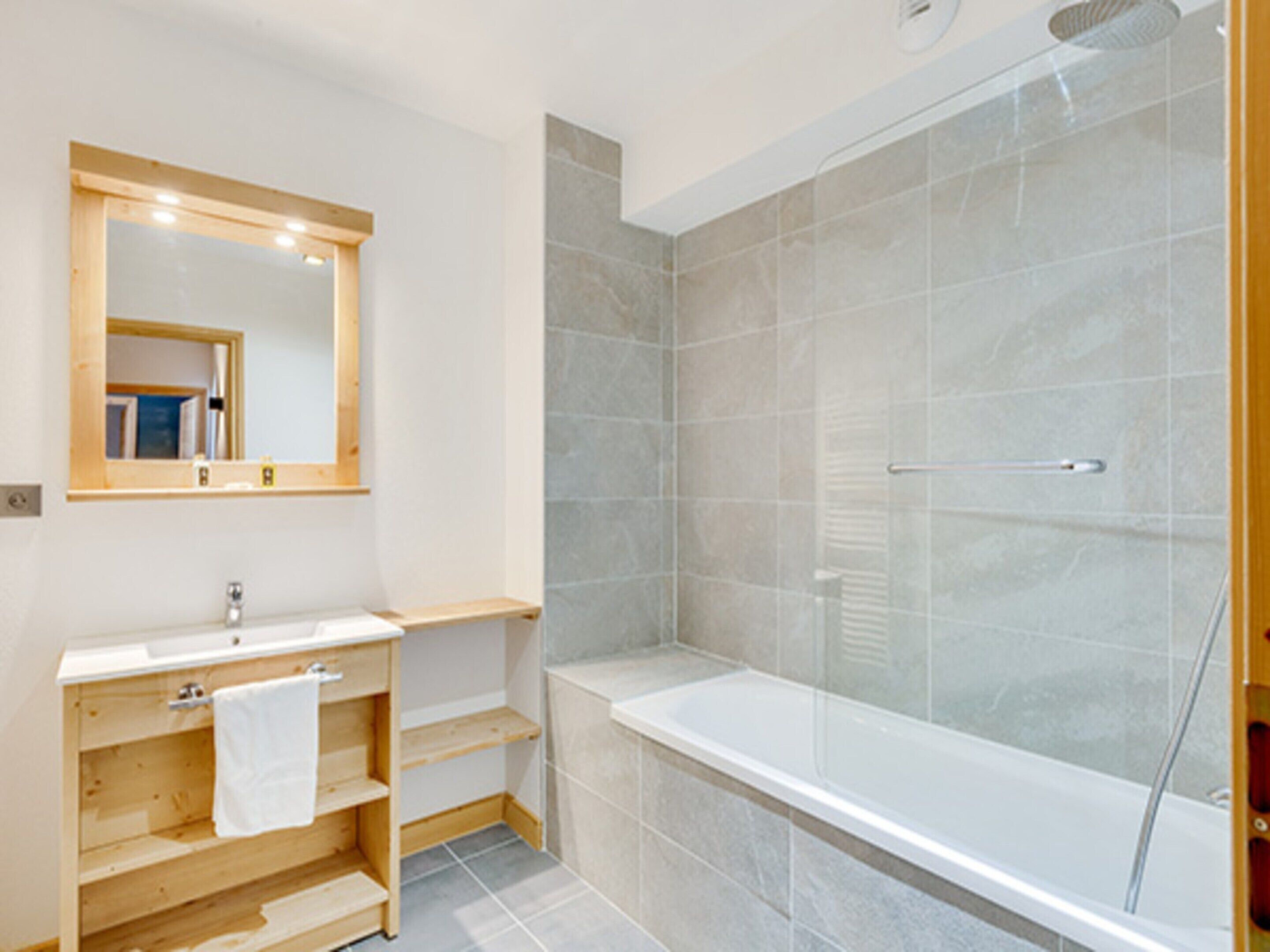 A modern bathroom with a wooden vanity, a large mirror, a bathtub, and a glass shower enclosure.