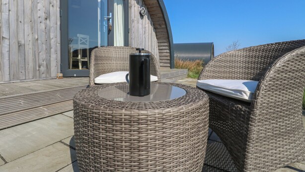 A wicker lounge chair with a table, a black thermos, and a sign reading "SCARBA" on a wooden building. - Losal (Oban)
