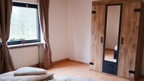 Un dormitorio con dos camas, una ventana con cortinas, un armario de madera y una lámpara en el techo.