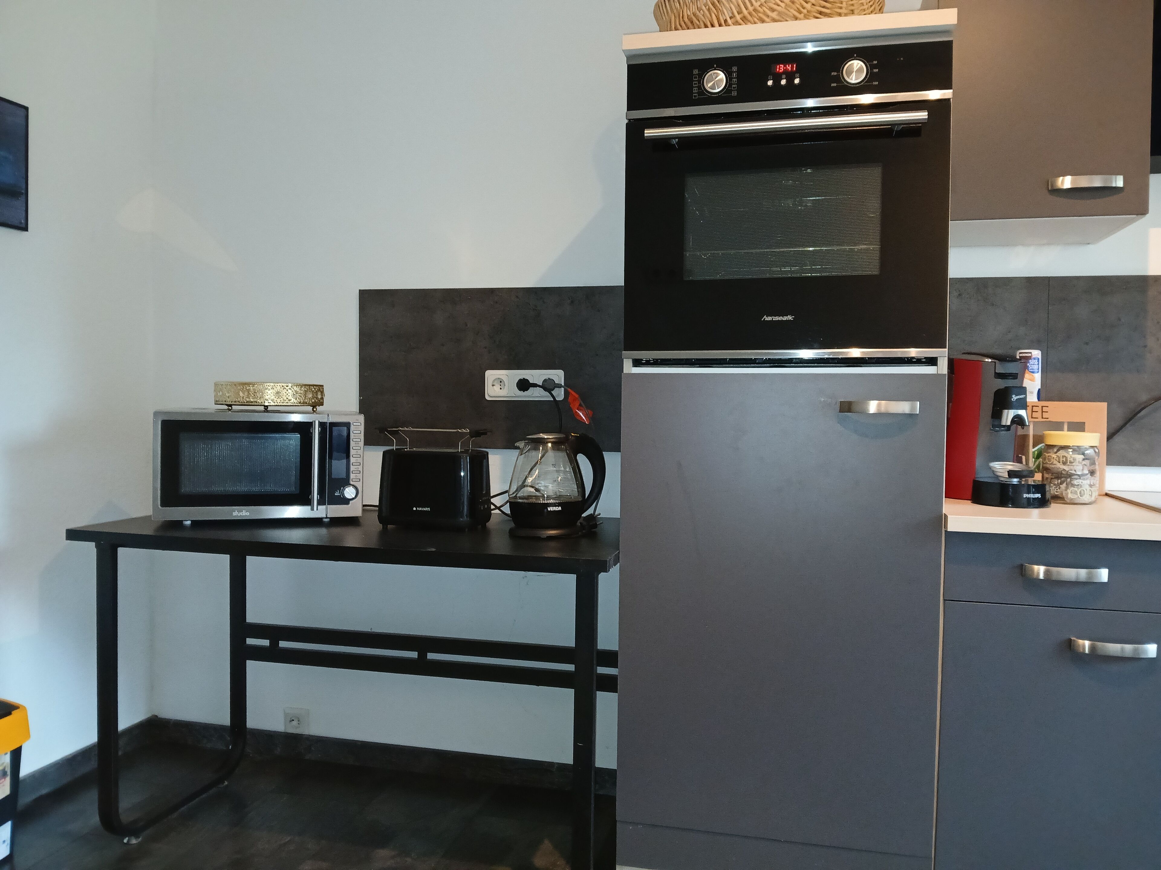 A compact kitchen with a microwave, toaster, and coffee maker on a black countertop.