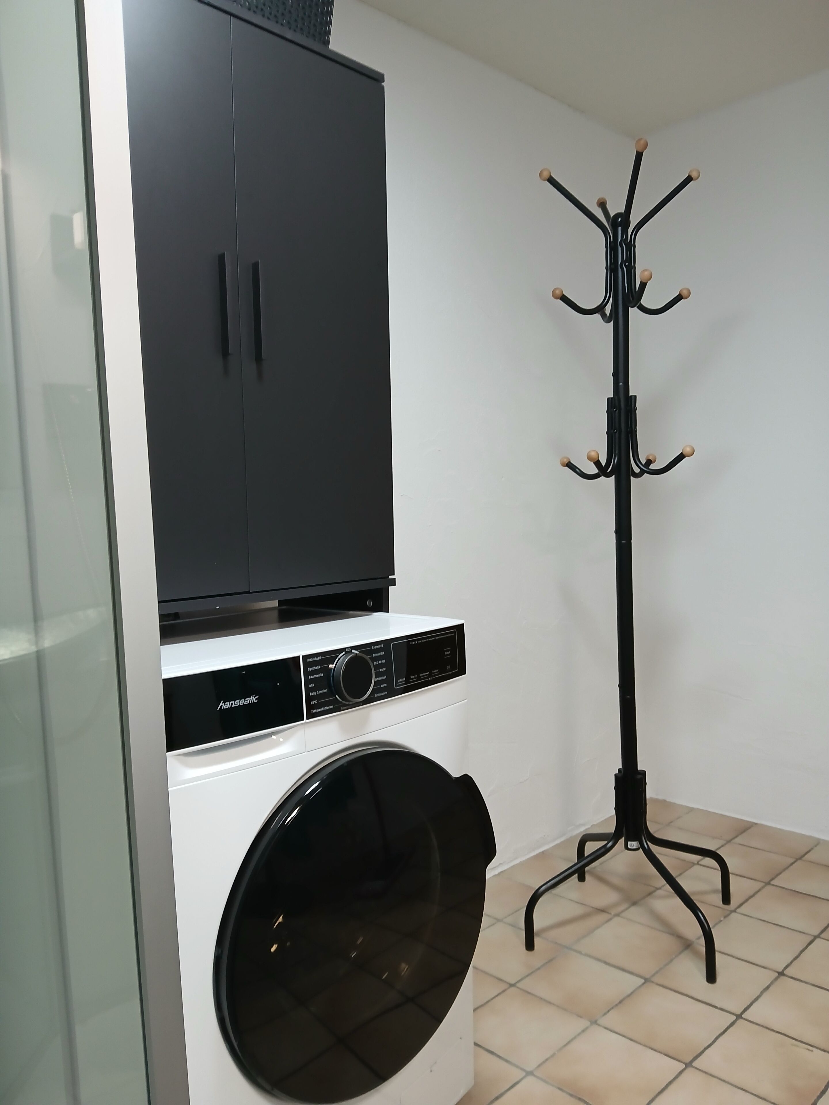 Uma área de lavanderia com máquina de lavar de abertura frontal, secadora e um armário sobre a secadora.