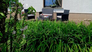 Un área de estar al aire libre con mobiliario de mimbre, una ventana y una pared blanca con textura.