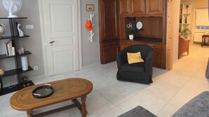 Una sala de estar con una mesa de centro de madera, un sillón negro con un cojín amarillo, una puerta blanca y armarios de madera.