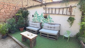 Un espacio exterior acogedor con mesa de madera, dos bancos acolchados y plantas en macetas.