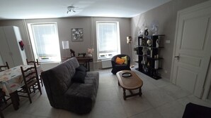 Una sala de estar con sofá, una mesa de centro, una mesa de comedor con sillas, una estantería y una puerta.