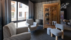 Een moderne woonkamer met stoelen met een hondentand patroon, een grijze poef en een houten kast met glazen deuren.