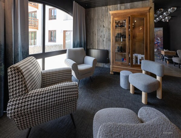 A modern living room with houndstooth patterned chairs, a grey ottoman, and a wooden cabinet with glass doors. - Charming Apartment Near Serre-chevalier (Saint-Chaffrey)