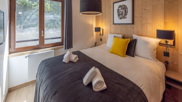 Ein Schlafzimmer mit einem großen Bett, zwei Nachttischlampen, einem gerahmten Bild an der Wand und einem Fenster mit Vorhängen.