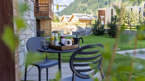 Een tafel met ontbijtartikelen en een koffiezetapparaat op een terras met uitzicht op een berg.