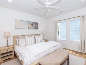 Cozy retreat with a large bed, ceiling fan, and a painting above, featuring a bedside table with lamps and a comfortable bench.