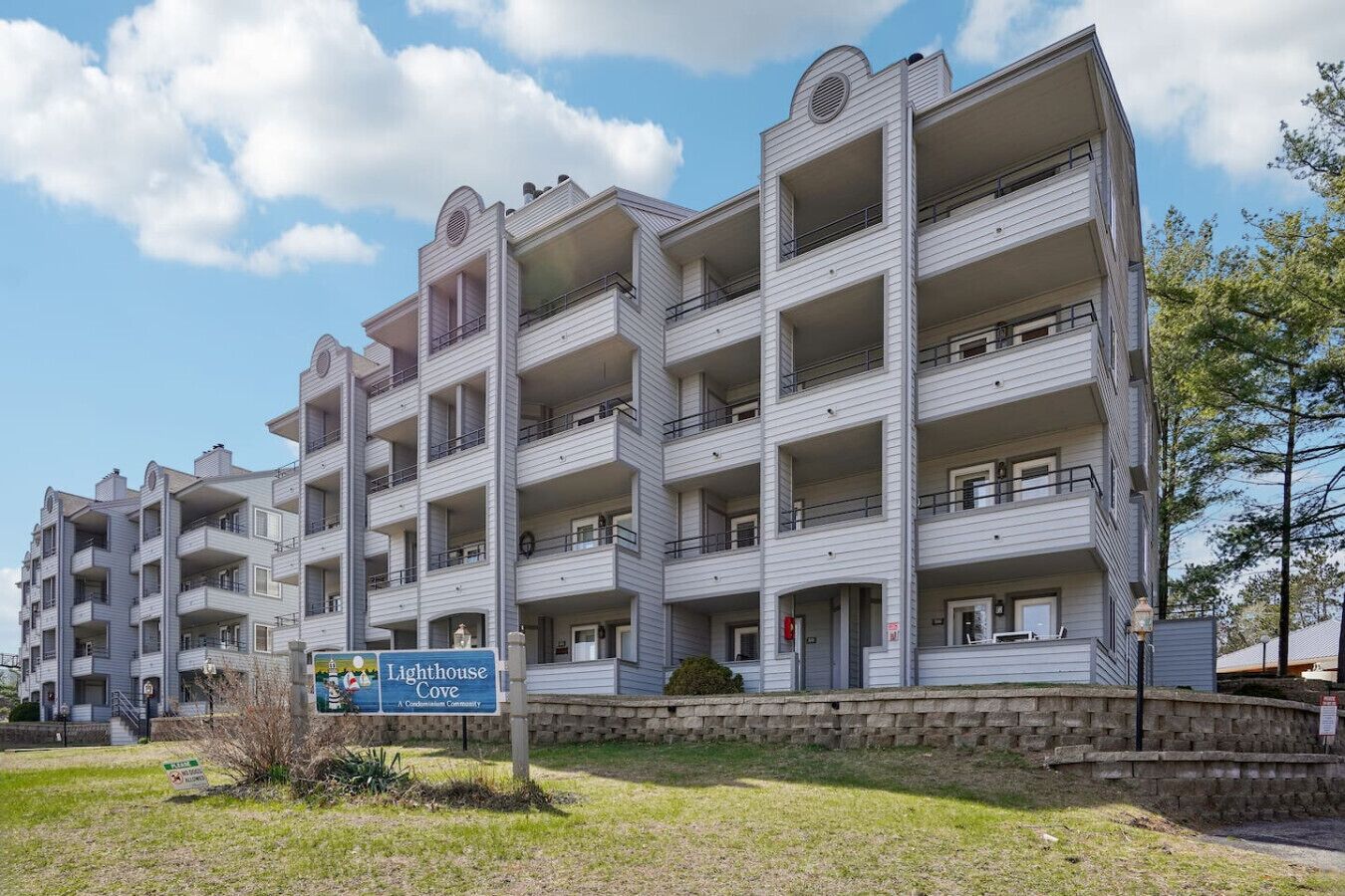 A multi-story building with balconies, a sign indicating it is a condominium community, and a stone wall in front.