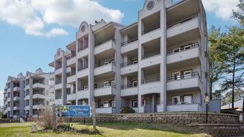 A multi-story building with balconies, a sign indicating it is a condominium community, and a stone wall in front.