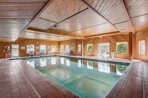 A large indoor swimming pool with wooden walls and ceiling, surrounded by lounge chairs and a clear view of the outside. - Pine Needle 506 at Lighthouse Cove (Wisconsin Dells)