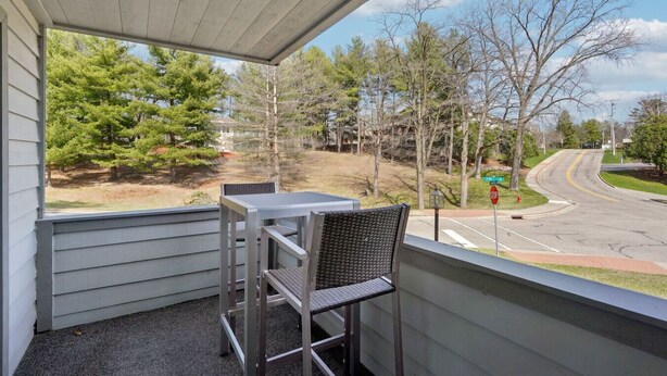 A balcony with a table and chairs, overlooking a street with trees and a stop sign. - Pine Needle 506 at Lighthouse Cove (Wisconsin Dells)