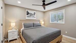 A bedroom with a bed, bedside tables, a ceiling fan, a window with blinds, and a framed picture on the wall. - Pine Needle 506 at Lighthouse Cove (Wisconsin Dells)