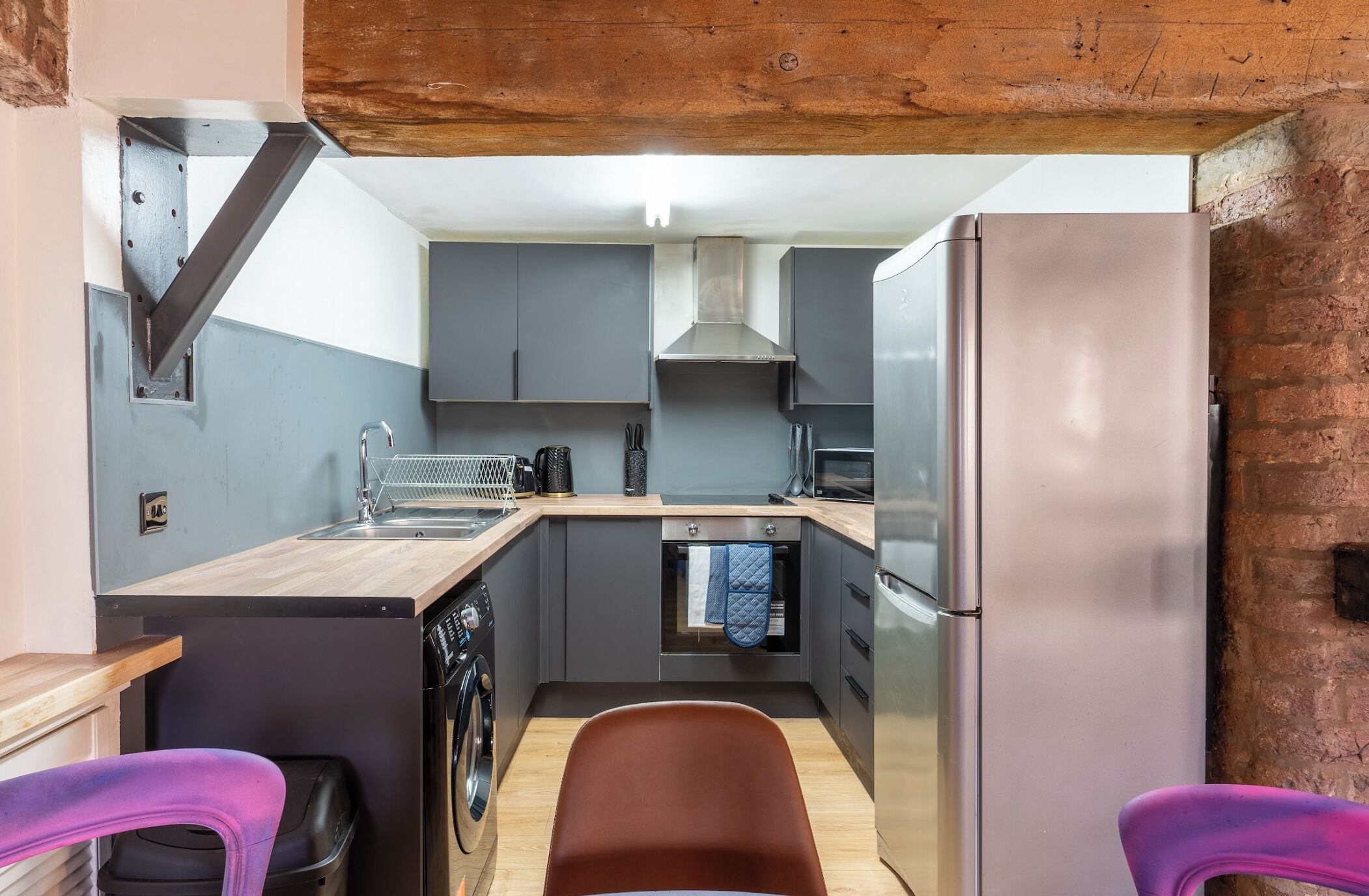Una cocina funcional con gabinetes grises, un refrigerador de acero inoxidable, horno integrado y lavadora.