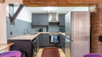 Una cocina funcional con gabinetes grises, un refrigerador de acero inoxidable, horno integrado y lavadora.