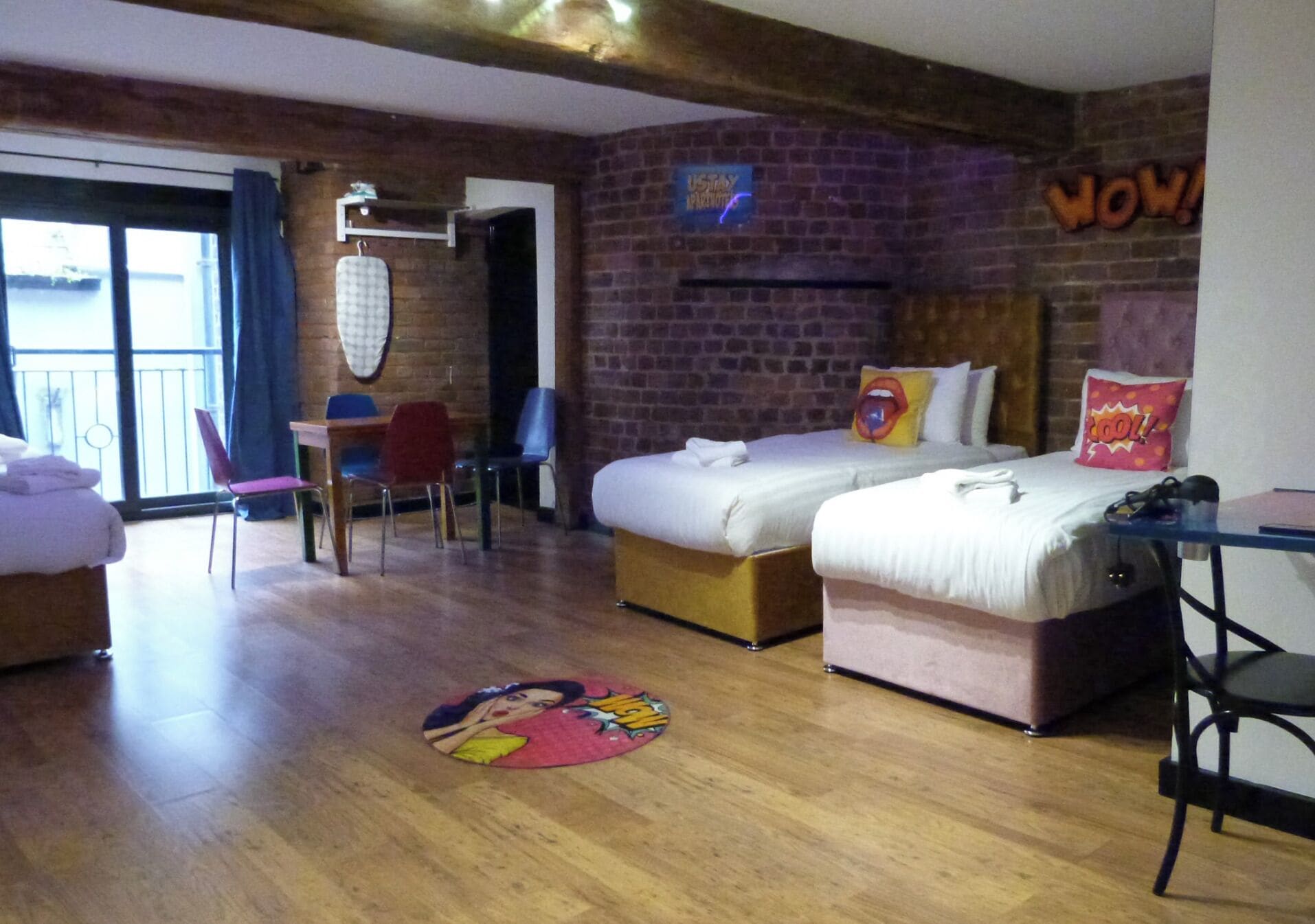 A hotel room with a brick wall, two beds, a desk, and a chair.