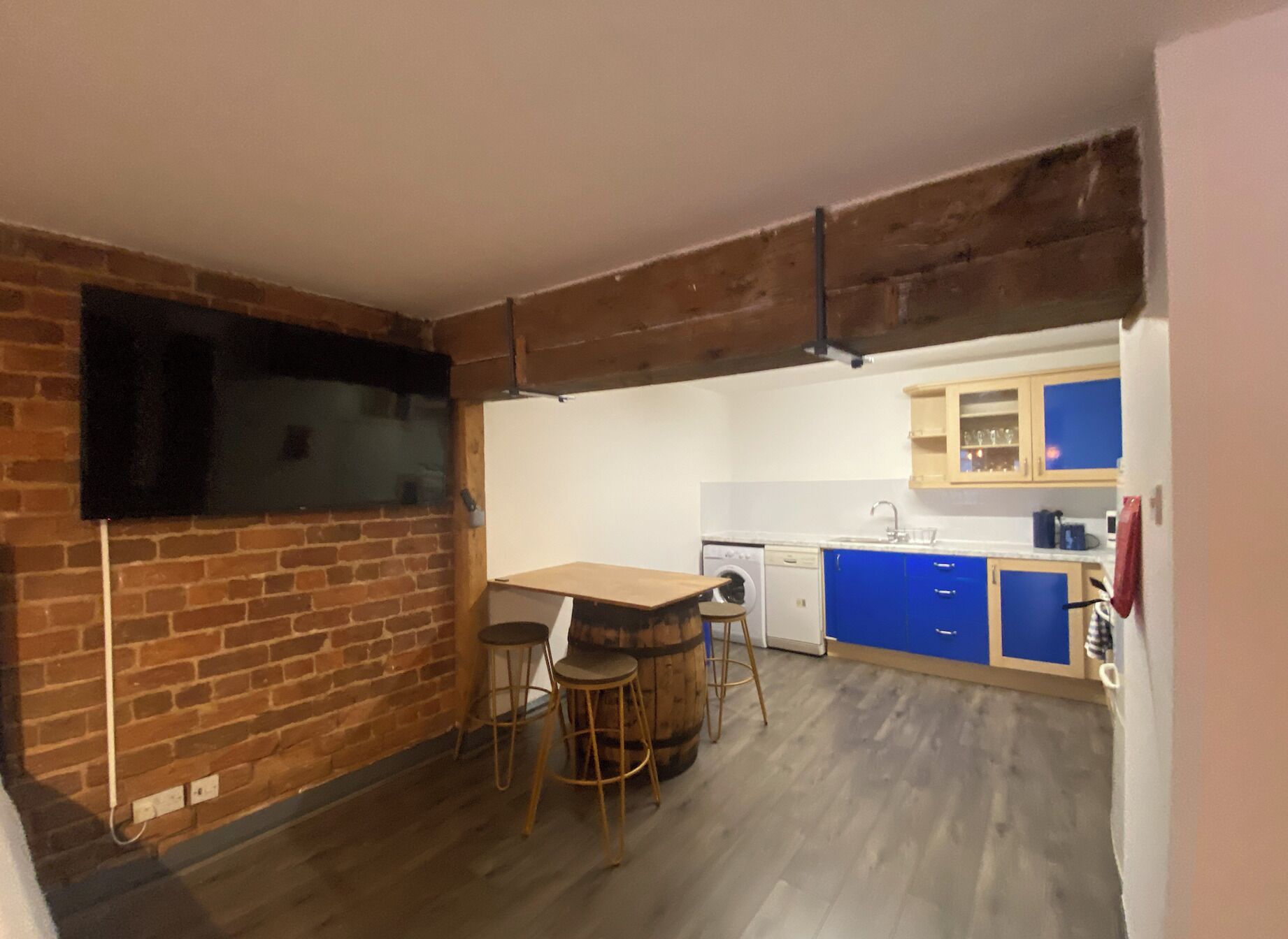 A kitchen with a brick wall, wooden table, stools, and blue cabinets.
