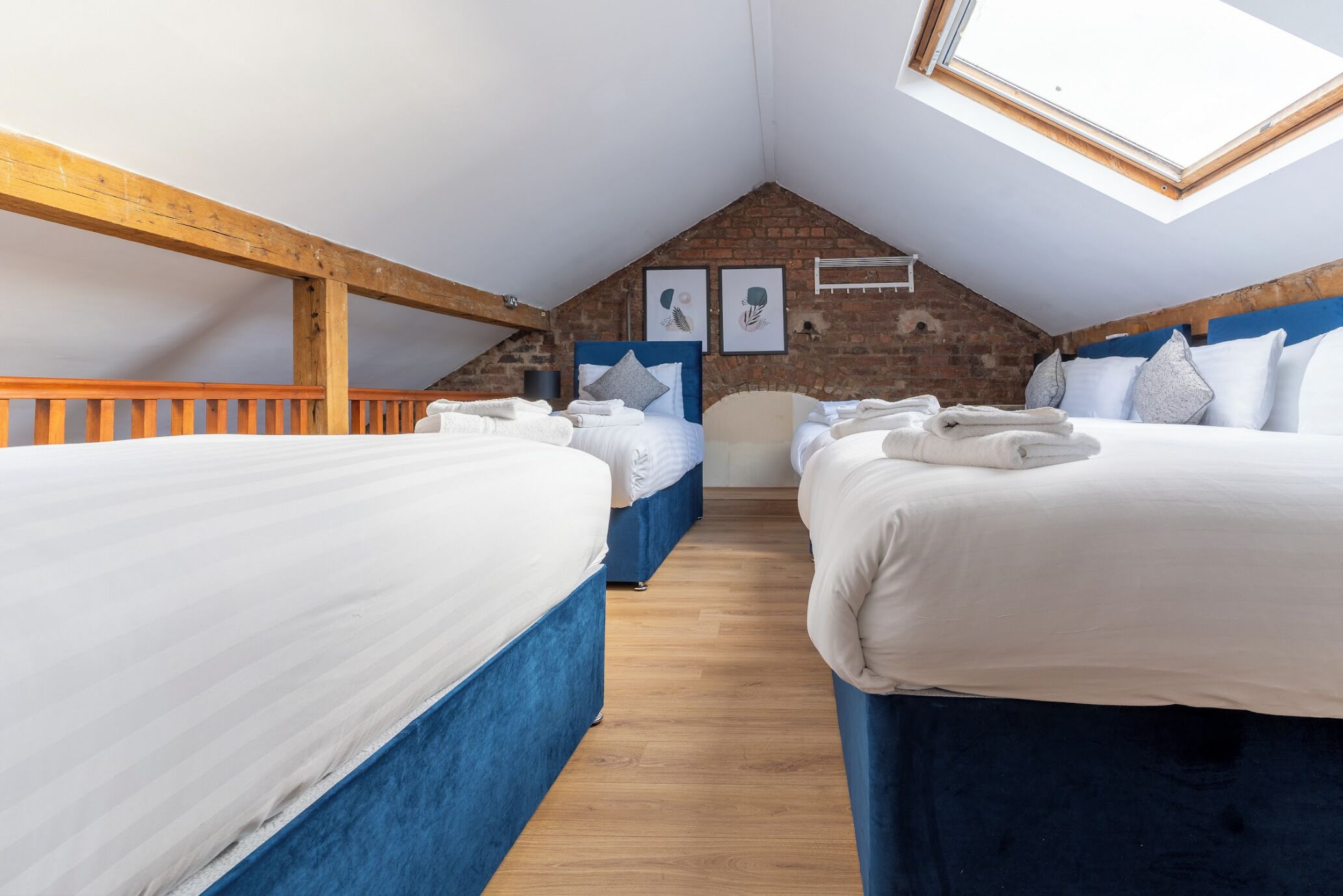 Une chambre confortable située sous les toits, avec deux lits, des poutres en bois, un plafond en pente et un puits de lumière.