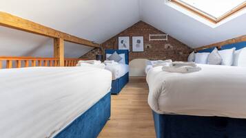 Une chambre confortable située sous les toits, avec deux lits, des poutres en bois, un plafond en pente et un puits de lumière.