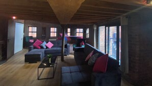Ein großzügiges Wohnzimmer mit hohen Decken, großen Fenstern und einer Mischung aus modernen und klassischen Möbeln.