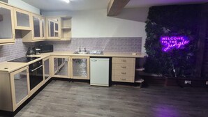 Eine Küche mit Holzausstattung, einer Mikrowelle, einem Toaster und einem Geschirrspüler. Ein Neonlichtschild trägt die Aufschrift 'WELCOME TO THE Jungle'.